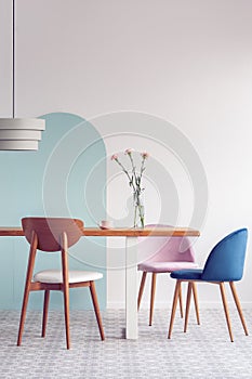 Pastel pink and petrol blue chairs at long wooden table in bright dining room