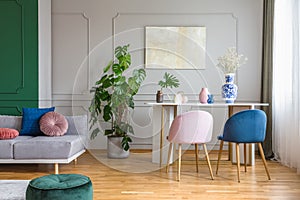 Pastel pink and petrol blue chairs at small dining table in bright living room