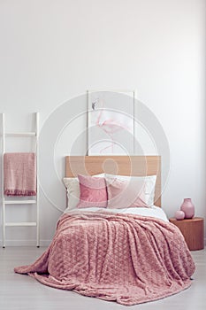Pastel pink pillow and blanket on single wooden bed with white bedding in scandinavian bedroom interior