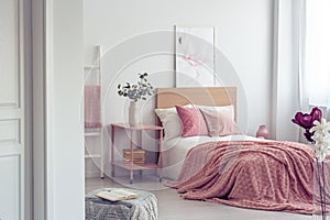 Pastel pink pillow and blanket on single wooden bed with white bedding in scandinavian bedroom interior