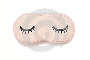 Pastel pink sleep mask with closed eyes embroidered on it with eyelashes on white background. Top view, flat lay.