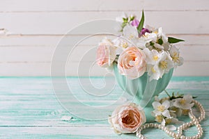 Pastel roses and jasmine flowers in vase on turquoise wooden b