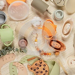 Pastel silicone collection of tableware, cutlery, bibs, accessories and wooden toys for children on cloth background.
