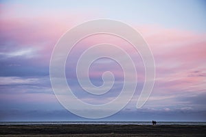 Pastel sky in south Iceland with two people walk on black sand b