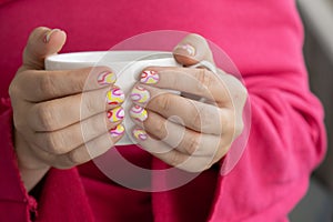 Pastel softness colorful manicured nails. Woman holding white cup of coffee or tea showing her new summer manicure in