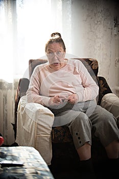 Pastimes. An elderly woman in glasses enjoys her hobby sitting in a armchair and knitting on the background of the