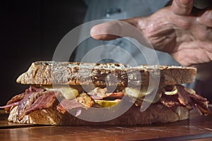 Pastrami sandwhich on a wooden tablet with delicious meet on baguette bread with cheese,copy space in parts of the image