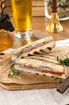 Pastrami sandwich on grilled bread with pickles and mustard on wooden table