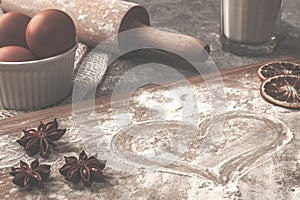 Pastry board with heart flour on the concrete countertop with eggs in the white bowl