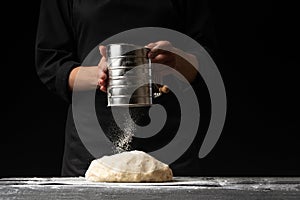 Pastry chef or baker cooks dough with flour, for sweets, rolls or Italian pizza or pasta. On a black background for design, for