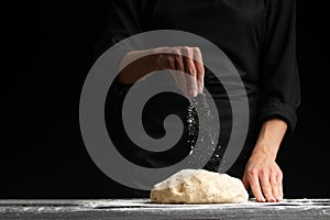 Pastry chef or baker cooks dough with flour, for sweets, rolls or Italian pizza or pasta. On a black background for design, for