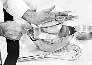 Pastry chef Baker sieving flour into a bowl in the kitchen of the bakery