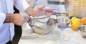 Pastry chef Baker sieving flour into a bowl in the kitchen of the bakery