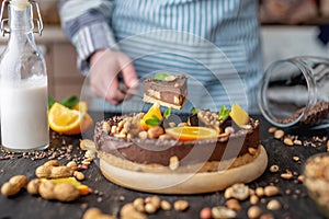 Pastry chef in hand holding a piece of chocolate cake with orange, mint and nuts. Healthy raw desserts for vegan food