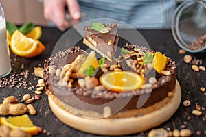 Pastry chef in hand holding a piece of chocolate cake with orange, mint and nuts. Healthy raw desserts for vegan food