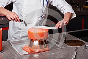 Pastry chef in the kitchen decorating a cake of orange glaze