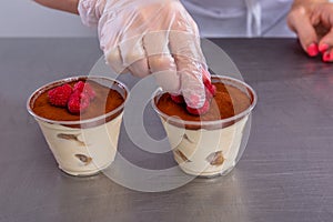 Pastry chef in the kitchen makes tiramisu with raspberries. Cook puts raspberries on the finished dessert. Master class in the