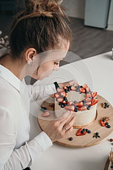 The pastry chef makes a cake at home. Delicious cream cheese cake with handmade berries. Girl learning to bake a cake