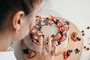 The pastry chef makes a cake at home. Delicious cream cheese cake with handmade berries. Girl learning to bake a cake