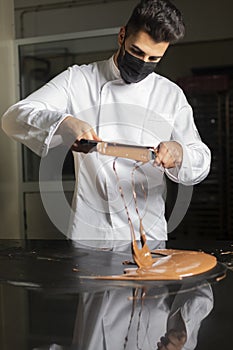 Pastry chef with mask working on tempering chocolate photo