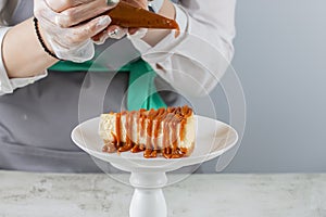 Pastry chef pours caramel on a slice of the freshest cheesecake on a white plate