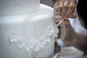 Pastry chef preparing a 3 tier frosted layered wedding cake decorated.