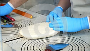 A pastry chef rolling out soft caramel in gloves on a table in a pastry shop.