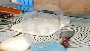 A pastry chef rolling out soft caramel with a rolling pin in a pastry shop.