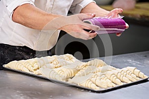 Pastry chef sealing with plastic film a tray of croissants dough.