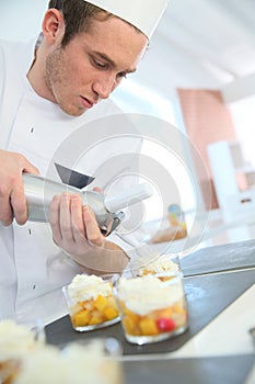 Pastry cook putting the whipped cream on desserts