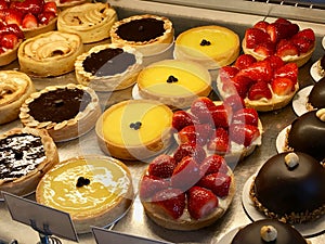 Pastry shop with variety of tarts, cakes, creme brulee, with strawberry, chocolate, lemon, pears and apple slices displayed at sho