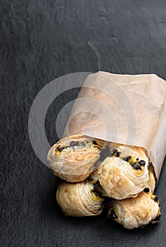 Pastry twists with a custard and dark chocolate chip filling in a paper bag on stone background