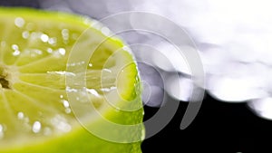 Patches of light of drops of water at a background. Drops of water fall on the cut lime on a black background. Limes Cut