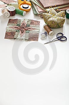 Patchwork block, stack of fabrics, sewing and quilting accessories. Copy space