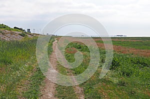 Path along grassy coastal marshland alone the ribble and alt estuary in merseyside looking towards southport with the pier in