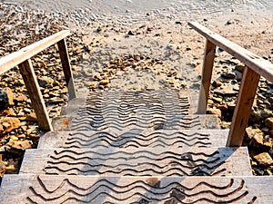 Path down to the beach. Empty wooden steps way on sandy beach, rock and sea water background.