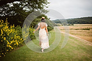 A path in a field of yellow flowers is graced by the presence of a woman strolling along it