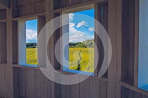 Path in the grass field through the wooden window view. Meadow picturesque summer landscape with clouds on blue marvelous sky