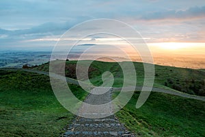 A path heading into the downhill. On the iron age hill fort of British Camp, Malvern Hills. With the the sun rising on a misty mor