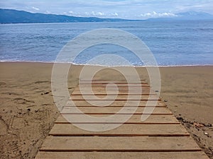 Path leading to the sand beach with sea waves, blue sky and clouds.