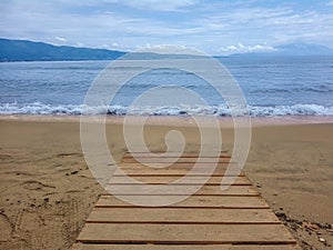 Path leading to the sand beach with sea waves, blue sky and clouds.