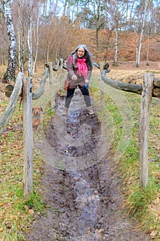 Path with mature woman trying to walk on muddy ground, dog looking at camara