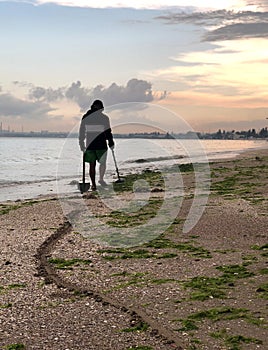 Path of a shovel behind a man searching for a precious metal using a metal detector on beach at sunset time