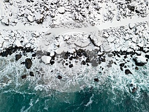 Path in the snow next to a wild shore with waves of blue ocean. Aerial view of dangerous winter pathway in Norway