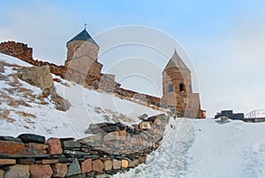 A path in the snow to ancient ortodox Gergeti Trinity church Tsminda Sameba against the stormy cloudy foggy sky at Caucasus mount