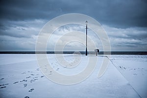 Path to enlightenment. Snow covered beach with footprints leading to antique lamp post.