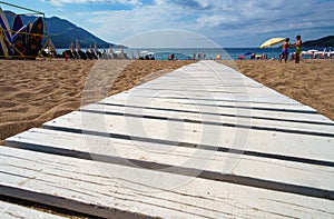 a path to the sea made of white boards, summer seaside in a resort town, a beach with sun loungers and umbrellas, a blue sunny sky