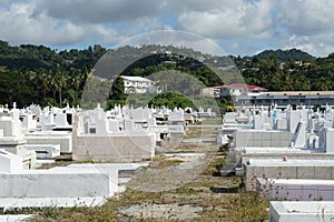 Path between white graves and tombstones in a cemetery near the beach in Castries, Saint Lucia.