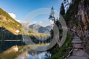 A path with a wooden fence climbs steeply beside the Braies lake