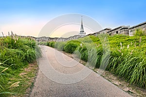 Pathway leading to an old stone wall beside modern skyscrapers under a clear sky at dusk, showcasing Seoul\'s urban landscape